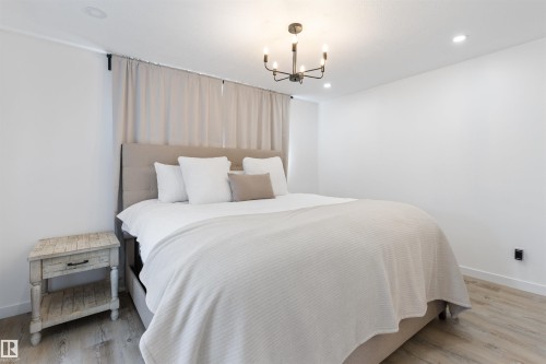 Bedroom featuring light wood-finish flooring, recessed lighting, a contemporary black chandelier, and a neutral upholstered headboard - 38 Woodcrest Avenue, St. Albert, AB - Indoor Photo Showing Bedroom