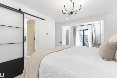 Room featuring a contemporary barn door with frosted glass panels, matte black chandelier, recessed lighting, and a double patio door with transom window - 38 Woodcrest Avenue, St. Albert, AB - Indoor Photo Showing Bedroom