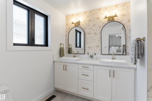 Dual vessel sinks set into a white countertop, featuring arched mirrors and brass sconces - 38 Woodcrest Avenue, St. Albert, AB - Indoor Photo Showing Bathroom