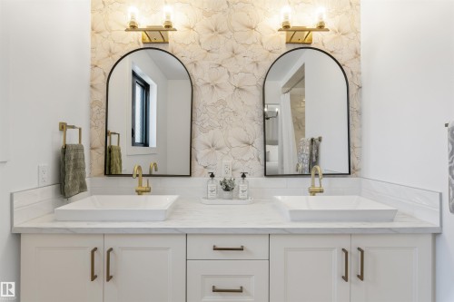 Dual vessel sinks set on a light-toned countertop, complemented by individual arched mirrors and brass-finish fixtures - 38 Woodcrest Avenue, St. Albert, AB - Indoor Photo Showing Bathroom