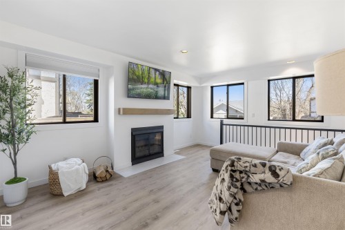 Living area featuring light wood-finish flooring, a contemporary fireplace with a light-toned mantel, multiple windows with dark frames, recessed lighting, and a dark metal railing - 38 Woodcrest Avenue, St. Albert, AB - Indoor Photo Showing Living Room With Fireplace