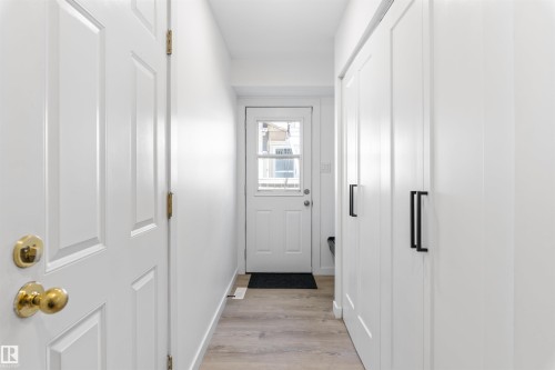 Foyer featuring light wood-finish flooring, white paneled doors with brass hardware, and built-in white cabinetry with black bar pulls - 38 Woodcrest Avenue, St. Albert, AB - Indoor Photo Showing Other Room