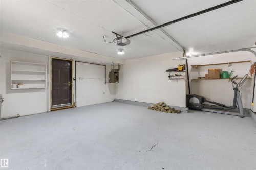 Spacious garage featuring a concrete floor, overhead lighting, garage door opener, interior access door, and built-in shelving - 38 Woodcrest Avenue, St. Albert, AB - Indoor Photo Showing Garage