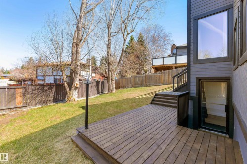 Expansive backyard featuring a large wood-finish deck, exterior stairs with dark railings, a ground-level walkout entrance, a manicured lawn, and mature trees - 38 Woodcrest Avenue, St. Albert, AB - Outdoor With Deck Patio Veranda