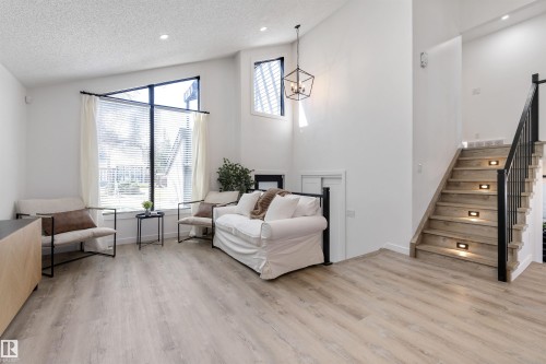 Bright living area featuring high ceilings, wood-finish flooring, and a contemporary staircase with integrated step lighting and black metal railing - 38 Woodcrest Avenue, St. Albert, AB - Indoor