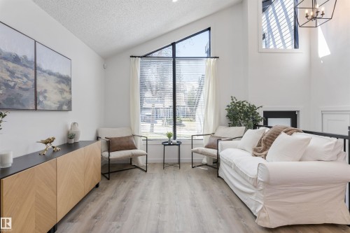 Living area featuring vaulted ceilings, large picture windows, wood-finish flooring, and a modern black linear chandelier - 38 Woodcrest Avenue, St. Albert, AB - Indoor