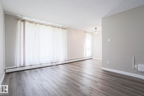 Spacious room featuring wood-finish flooring, light grey painted walls, and ample natural light from multiple windows - 118 7220 144 Avenue, Edmonton, AB - Indoor Photo Showing Other Room