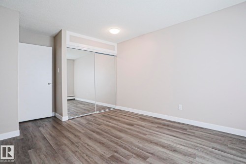 Room featuring wood-finish flooring, a wall-to-wall mirrored closet with sliding doors, and neutral wall tones - 118 7220 144 Avenue, Edmonton, AB - Indoor Photo Showing Other Room