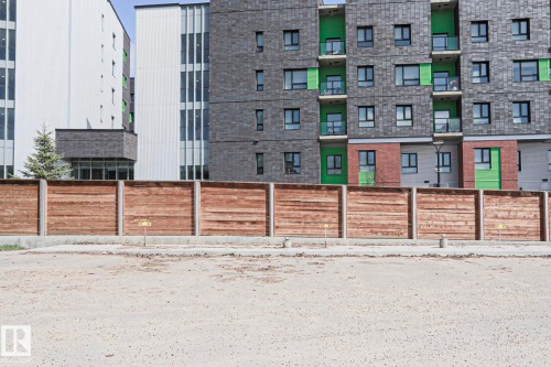 Multi-story building featuring a facade of grey stone paneling with vibrant green accent panels and brickwork - 118 7220 144 Avenue, Edmonton, AB - Outdoor With Facade