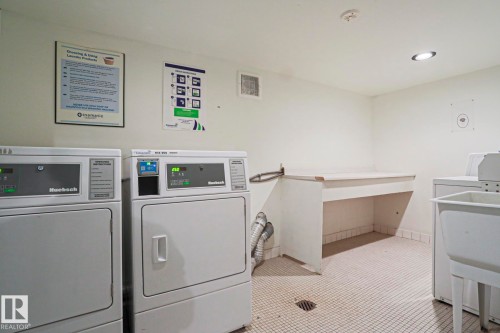 Dedicated laundry room featuring multiple washing machines and dryers, a utility sink, and a built-in folding counter - 118 7220 144 Avenue, Edmonton, AB - Indoor Photo Showing Laundry Room