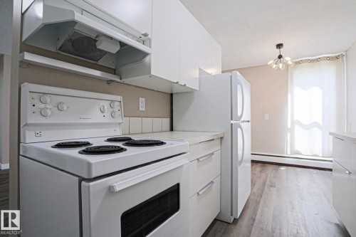 Kitchen featuring white appliances, white cabinetry, light countertops, wood-finish flooring, and an overhead light fixture - 118 7220 144 Avenue, Edmonton, AB - Indoor Photo Showing Kitchen