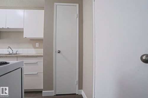 White kitchen cabinetry with integrated hardware, a stainless steel sink, and a tiled backsplash - 118 7220 144 Avenue, Edmonton, AB - Indoor