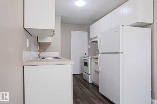 Kitchen featuring white cabinetry, wood-finish flooring, a stainless steel sink, and white appliances - 118 7220 144 Avenue, Edmonton, AB - Indoor Photo Showing Kitchen