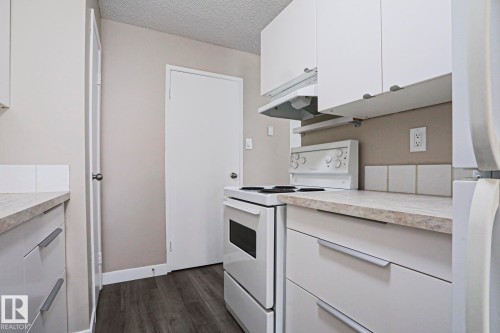 Galley-style kitchen featuring white cabinetry with modern pulls, a white electric range, and laminate countertops - 118 7220 144 Avenue, Edmonton, AB - Indoor Photo Showing Kitchen