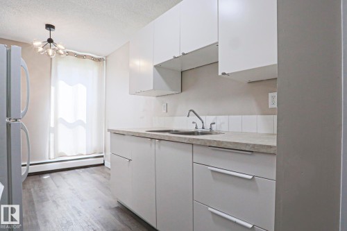 Kitchen featuring white cabinetry with integrated hardware, a double basin stainless steel sink, and a light-toned countertop - 118 7220 144 Avenue, Edmonton, AB - Indoor Photo Showing Kitchen