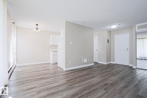 Spacious open-concept living area featuring wood-finish flooring, a contemporary ceiling light fixture, and white baseboards - 118 7220 144 Avenue, Edmonton, AB - Indoor Photo Showing Other Room