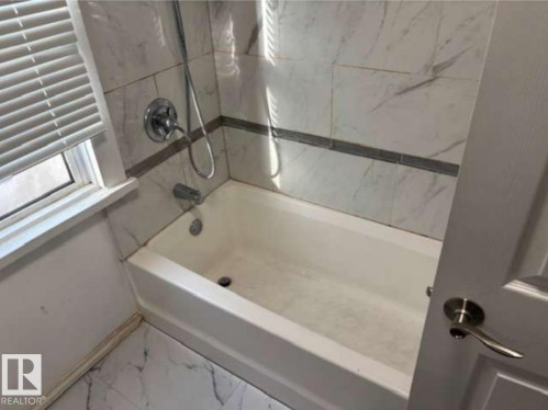 Bathroom featuring a white bathtub, white and gray veined tile surround, and a coordinating tile floor - 10730 92 Street, Edmonton, AB - Indoor Photo Showing Bathroom