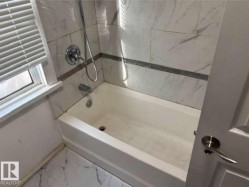 Bathroom featuring a white bathtub, white and gray veined tile surround, and a coordinating tile floor - 