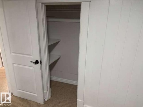 Closet with built-in shelving, white paneled walls, white trim, and a black lever door handle - 10730 92 Street, Edmonton, AB - Indoor Photo Showing Other Room