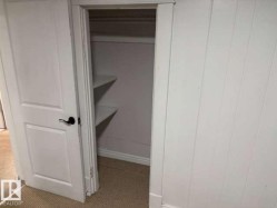 Closet with built-in shelving, white paneled walls, white trim, and a black lever door handle - 