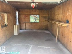 Garage interior featuring plywood wall finishes, concrete flooring, and built-in shelving - 