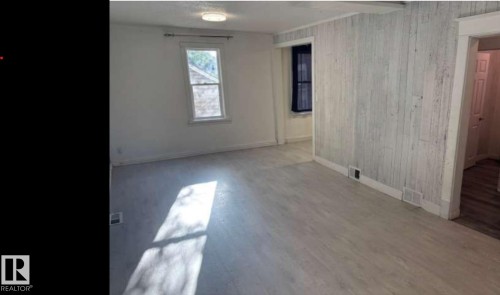 Spacious room featuring light-toned wood-finish flooring, white painted walls, and a prominent shiplap accent wall - 10730 92 Street, Edmonton, AB - Indoor Photo Showing Other Room