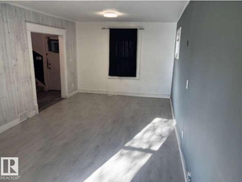 Spacious interior featuring light wood-finish flooring, a white textured accent wall, and a contrasting gray painted wall - 10730 92 Street, Edmonton, AB - Indoor Photo Showing Other Room