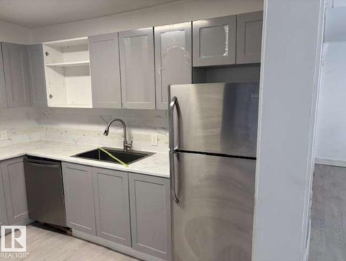 Kitchen featuring light gray shaker cabinetry, white stone-finish countertops, stainless steel appliances, and a matte black sink with a gooseneck faucet - 10730 92 Street, Edmonton, AB - Indoor Photo Showing Kitchen