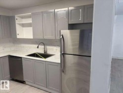 Kitchen featuring light gray shaker cabinetry, white stone-finish countertops, stainless steel appliances, and a matte black sink with a gooseneck faucet - 