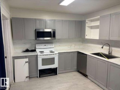 Kitchen featuring grey shaker-style cabinetry, light-toned countertops with a matching backsplash, and wood-finish flooring - 10730 92 Street, Edmonton, AB - Indoor Photo Showing Kitchen