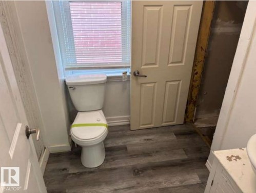 Bathroom featuring a white toilet, wood-finish flooring, and a window with blinds - 10730 92 Street, Edmonton, AB - Indoor Photo Showing Bathroom