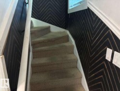 Staircase featuring carpeted treads and risers, white painted balustrade, and a dark accent wall with a chevron pattern - 
