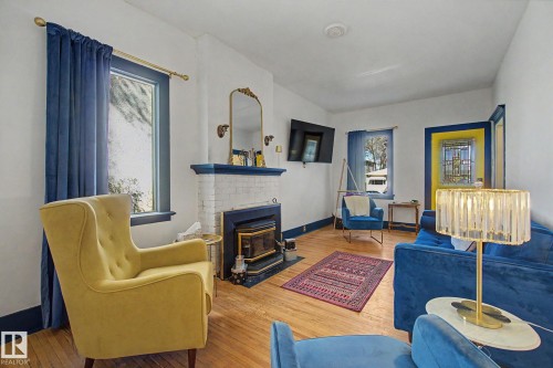 Hardwood flooring throughout a living space featuring a white brick fireplace with a dark blue mantel - 11512 122 St, Edmonton, AB - Indoor Photo Showing Living Room With Fireplace