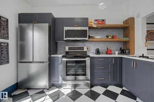 Kitchen featuring stainless steel appliances, black and white checkered flooring, matte gray cabinetry with gold-toned hardware, white countertops, and a gray subway tile backsplash - 11512 122 St, Edmonton, AB - Indoor Photo Showing Kitchen