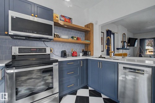 Contemporary kitchen featuring blue cabinetry with gold-toned hardware, stainless steel appliances, and a checkerboard floor - 11512 122 St, Edmonton, AB - Indoor Photo Showing Kitchen