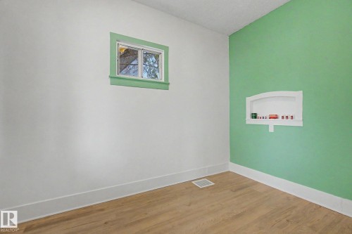 Room with wood-finish flooring, white baseboards, and a window with green trim - 11512 122 St, Edmonton, AB - Indoor Photo Showing Other Room