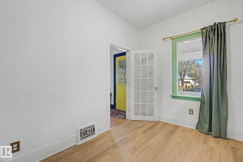 Room featuring wood-finish flooring, white walls, and a window with green trim - 11512 122 St, Edmonton, AB - Indoor Photo Showing Other Room