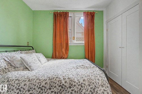Room with wood-finish flooring featuring a window with natural light and built-in white bifold closet doors - 11512 122 St, Edmonton, AB - Indoor Photo Showing Bedroom