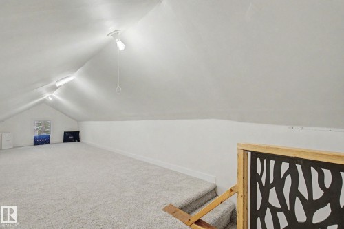 Spacious room featuring vaulted ceilings, light-hued carpeting, a single window, and a built-in stairwell partition with a decorative panel - 11512 122 St, Edmonton, AB - Indoor Photo Showing Other Room