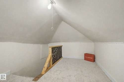 Carpeted loft space with angled ceilings, light-toned walls, and a wood-framed railing with a decorative metal insert - 11512 122 St, Edmonton, AB - Indoor Photo Showing Other Room