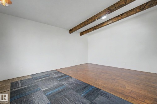Exposed wood-finish ceiling beams with recessed lighting, white walls, and a combination of wood-finish flooring and patterned carpet tiles - 11512 122 St, Edmonton, AB - Indoor Photo Showing Other Room