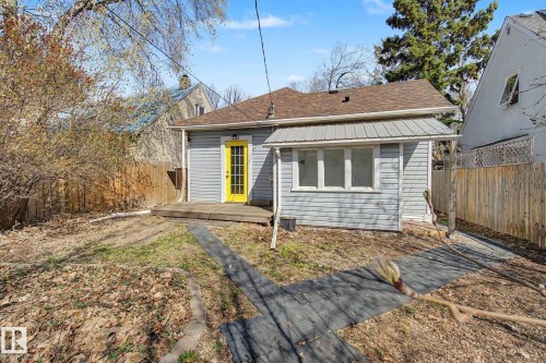Rear exterior featuring light blue siding, a brown shingle roof, a bright yellow door, and a wooden deck - 11512 122 St, Edmonton, AB - Outdoor