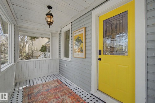 Covered front porch featuring a vibrant yellow entry door with decorative glass, black and white hexagon tile flooring, and a traditional hanging lantern - 11512 122 St, Edmonton, AB -  With Exterior
