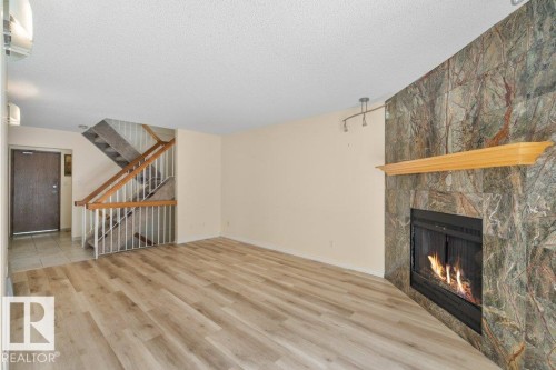 Living area featuring wood-look flooring, a fireplace with a stone surround and a wooden mantel, and a visible staircase with wooden handrails - 17313 60 Avenue, Edmonton, AB - Indoor With Fireplace