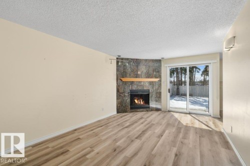 Living room with light-toned flooring, a fireplace featuring a stone surround, and glass sliding doors providing access to the outdoors - 17313 60 Avenue, Edmonton, AB - Indoor Photo Showing Living Room With Fireplace