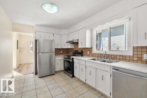 The kitchen features white cabinetry, a tiled backsplash, and stainless steel appliances - 17313 60 Avenue, Edmonton, AB - Indoor Photo Showing Kitchen With Double Sink