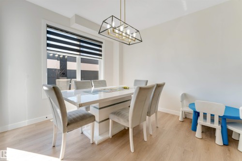 Dining area featuring wood-finish flooring, a contemporary linear chandelier with a black frame and gold accents, and a large window with horizontal banded blinds - 7007 169 Avenue Nw, Edmonton, AB - Indoor Photo Showing Dining Room