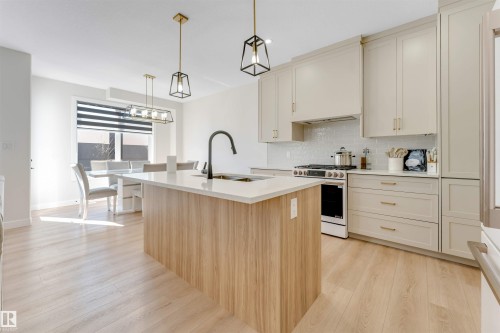 Open-concept kitchen featuring light wood-finish flooring, a central island with a white countertop and dark gooseneck faucet, light-toned cabinetry, and a white subway tile backsplash - 7007 169 Avenue Nw, Edmonton, AB - Indoor Photo Showing Kitchen With Upgraded Kitchen