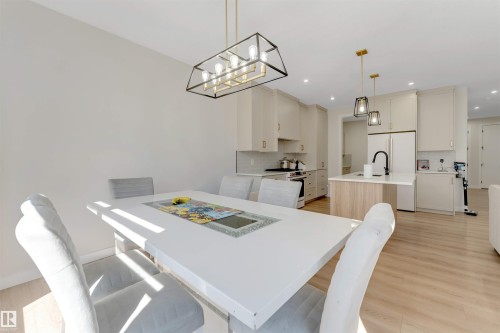 Open-concept dining area featuring a modern chandelier, light wood-finish flooring, and white walls - 7007 169 Avenue Nw, Edmonton, AB - Indoor