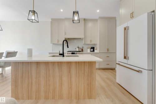 Kitchen featuring a wood-finish island with a light-toned countertop, white cabinetry with gold-toned hardware, a white subway tile backsplash, and light wood-finish flooring - 7007 169 Avenue Nw, Edmonton, AB - Indoor Photo Showing Kitchen
